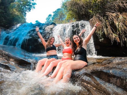 three girls sitting in a waterfall on a rock in swimwear 