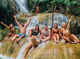 Group sitting amongst a waterfall with hands in the air