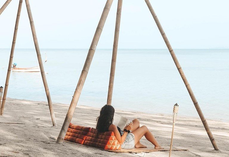Girl relaxing on beach reading a book lounging on the sand in Thailand