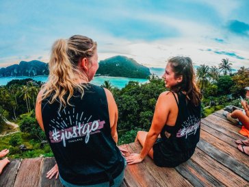 Two girls wearing TruTravels vests sitting at viewpoint in PhiPhi, Thailand with the ocean and islands in front of them