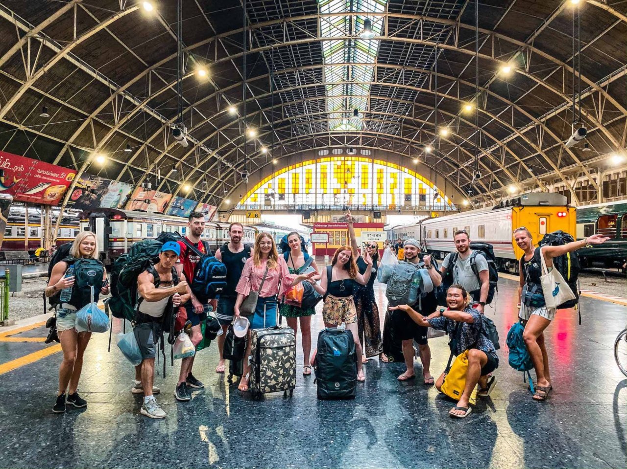 Group at train station in Bangkok with all their backpacks and bags and trains in the background