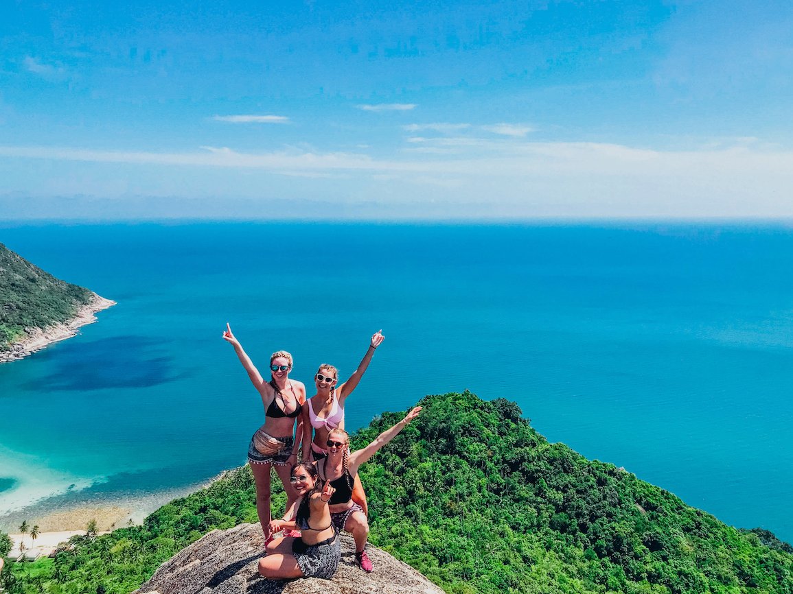 Girls with hands up on rock view point with the sea in the background