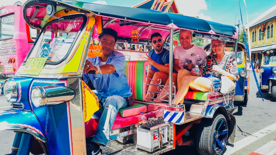 Colourful Tuk Tuk ride with driver and 3 people sat in the back exploring Bangkok in heart of Thailand