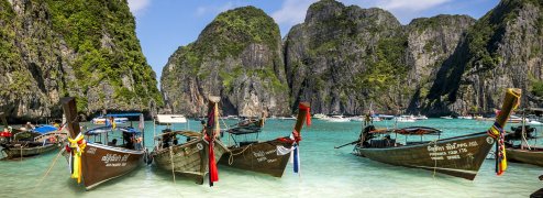 Longtail boats in Thailand at shore with turquoise waters and limestone cliffs in background